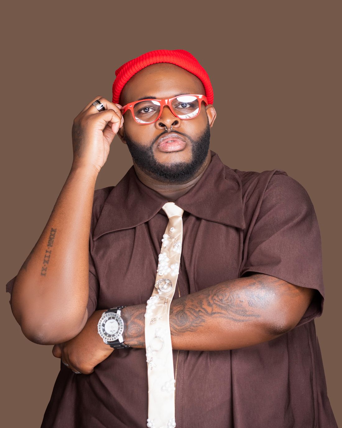 Jay Washington adjusting red glasses, in a brown shirt and pearl-embellished tie